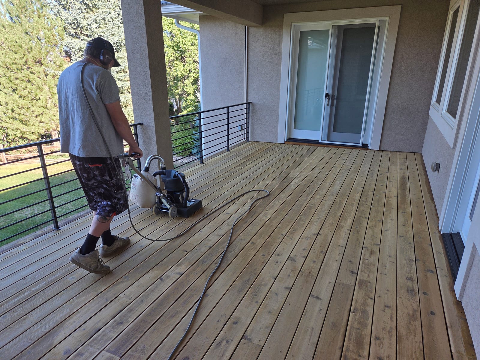 Technician operating a sanding machine across bare deck boards