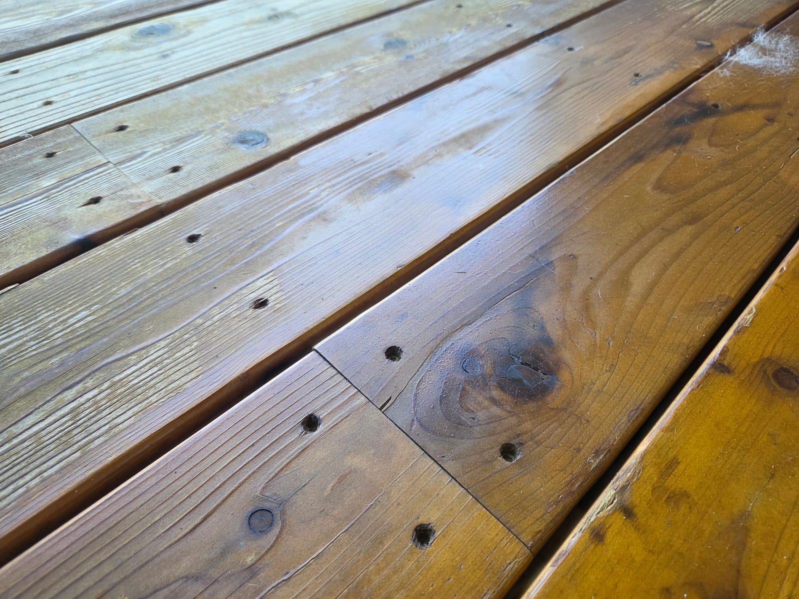 Close-up of deck boards showing bare stripped wood on the left next to boards still holding sticky old film-forming stain on the right