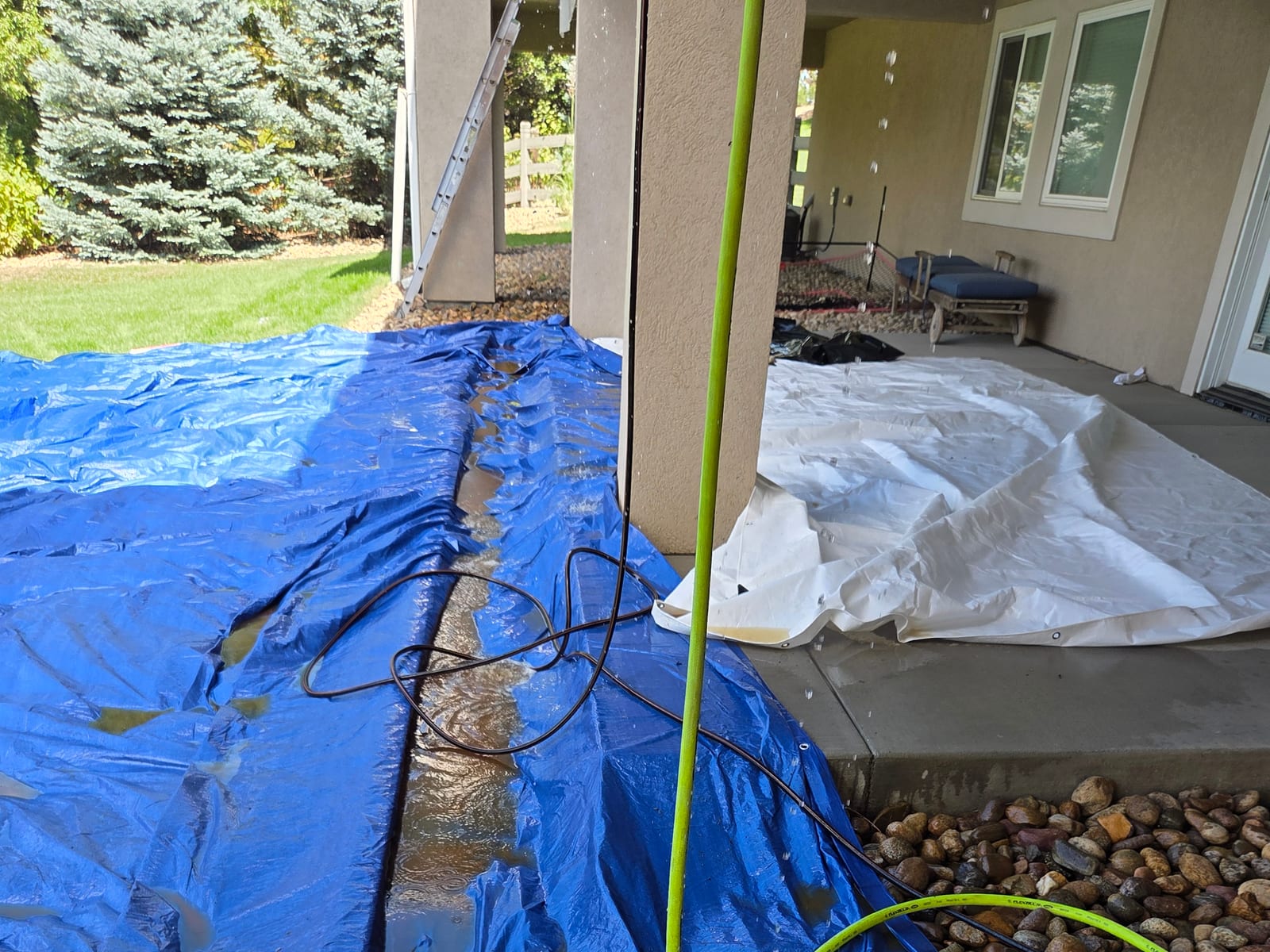 Blue tarp covering landscaping and railing to protect surroundings during deck stripping