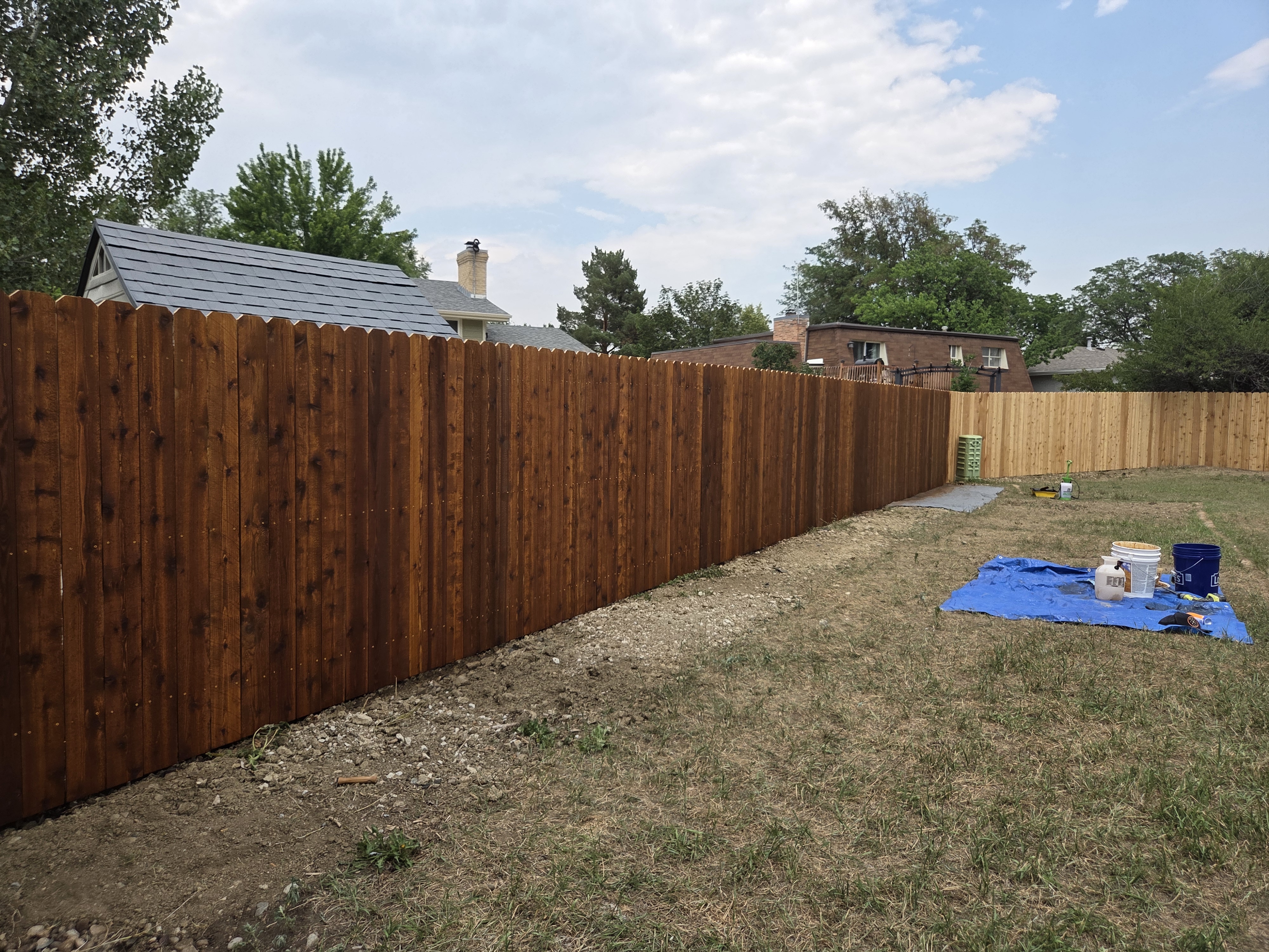 Looking down the length of a freshly stained cedar fence with gravel border