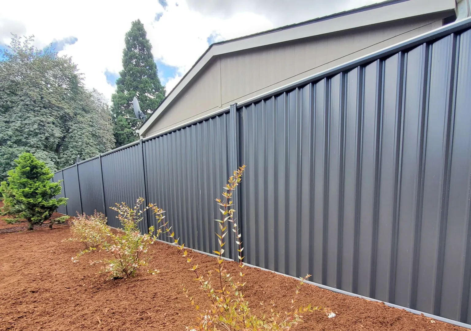Noncombustible steel fence section attached directly to a house, transitioning to wood fencing further from the structure