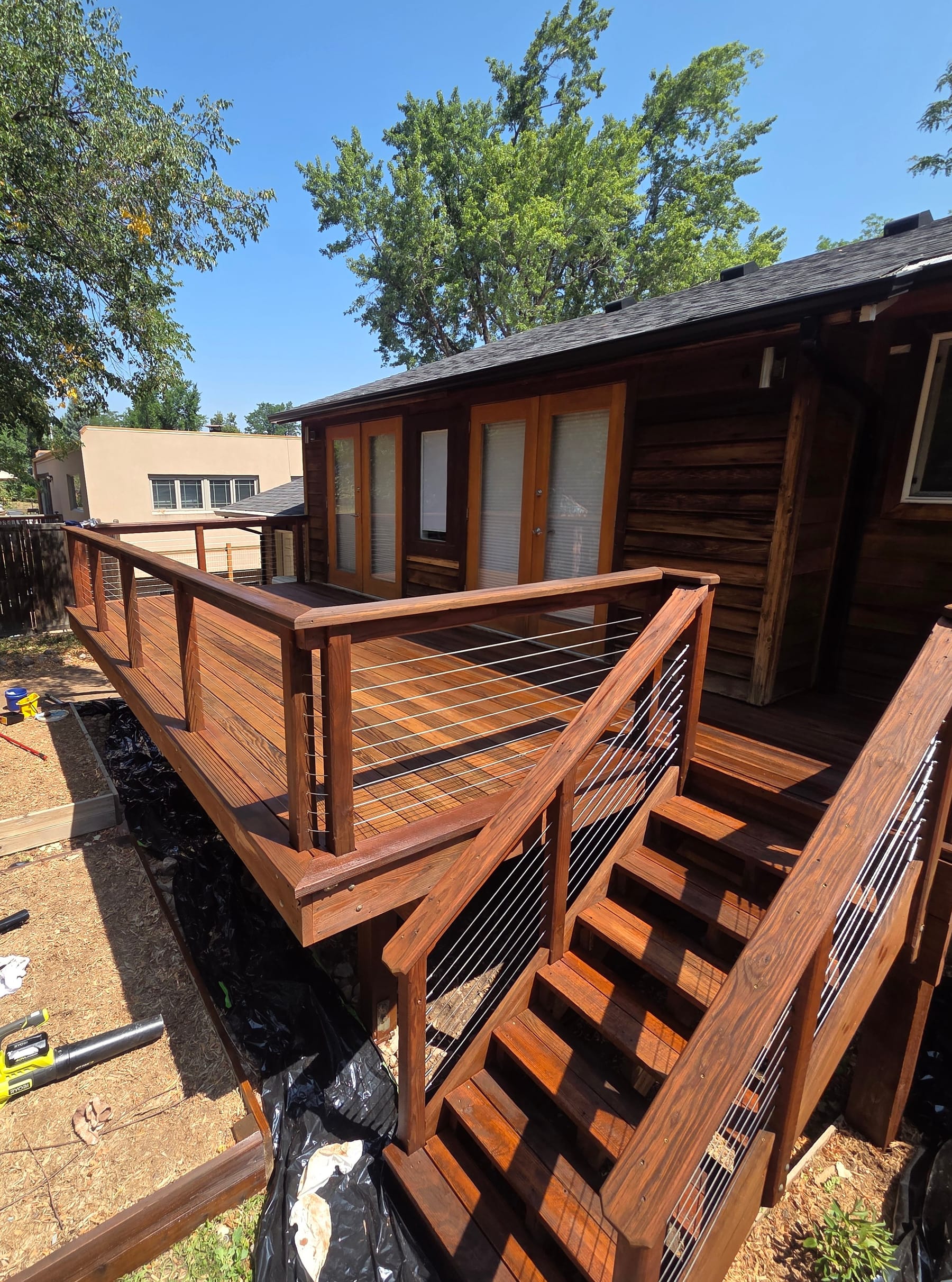 Finished wood deck with cable railing and staircase leading up to French doors