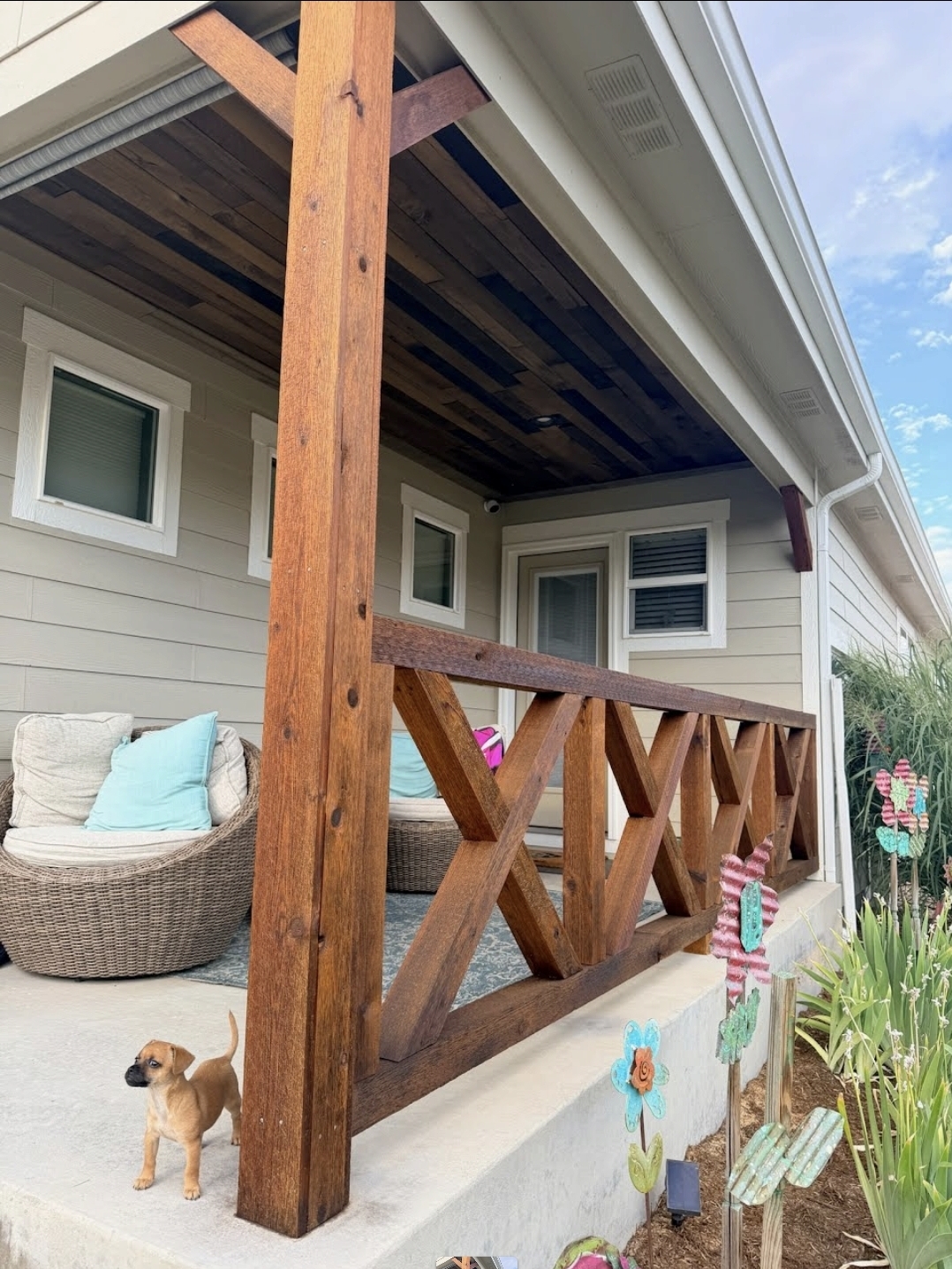 Stained wood porch railing with X-brace design and matching stained ceiling boards