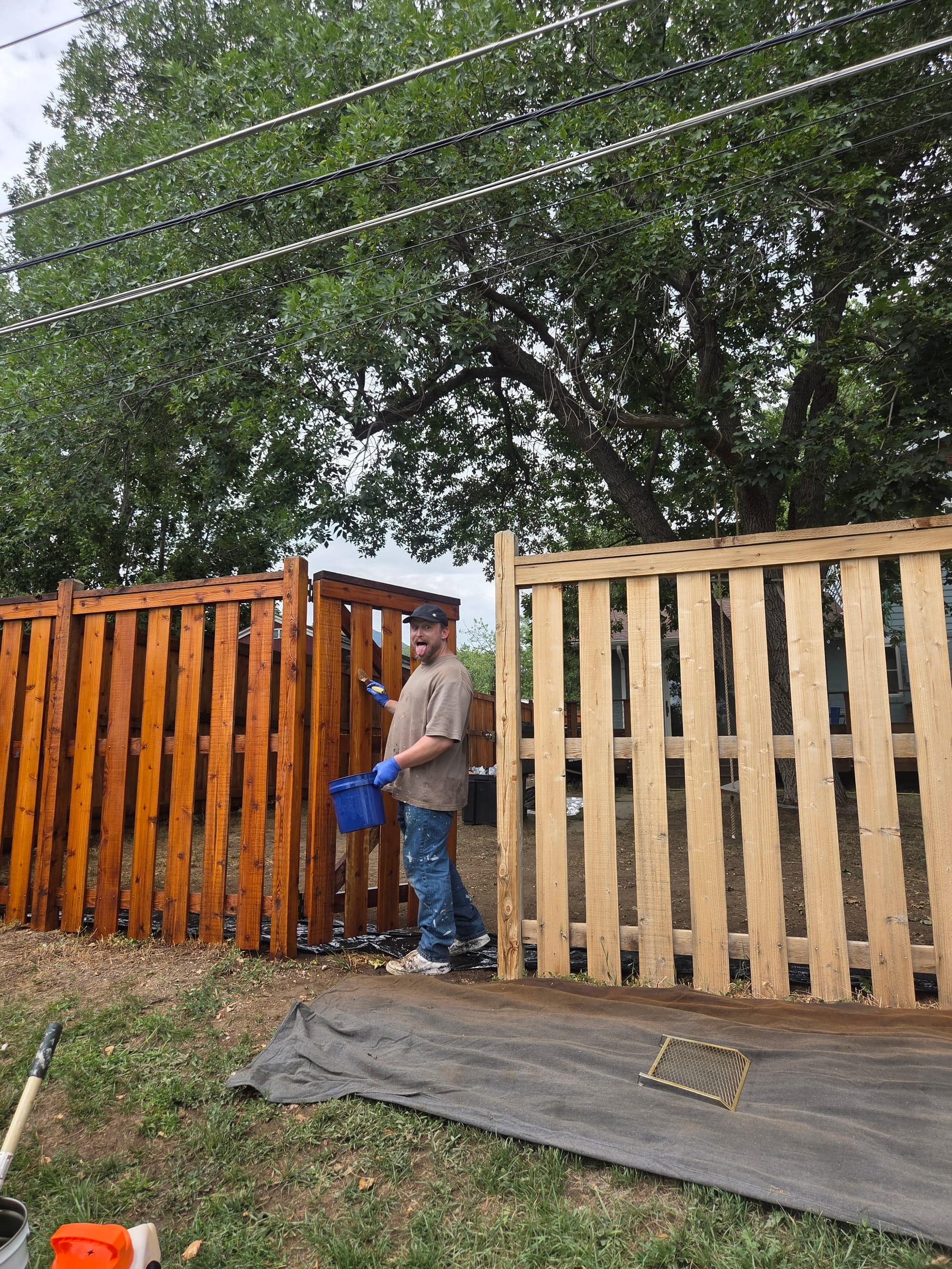 Crew member hand-staining a wood privacy screen